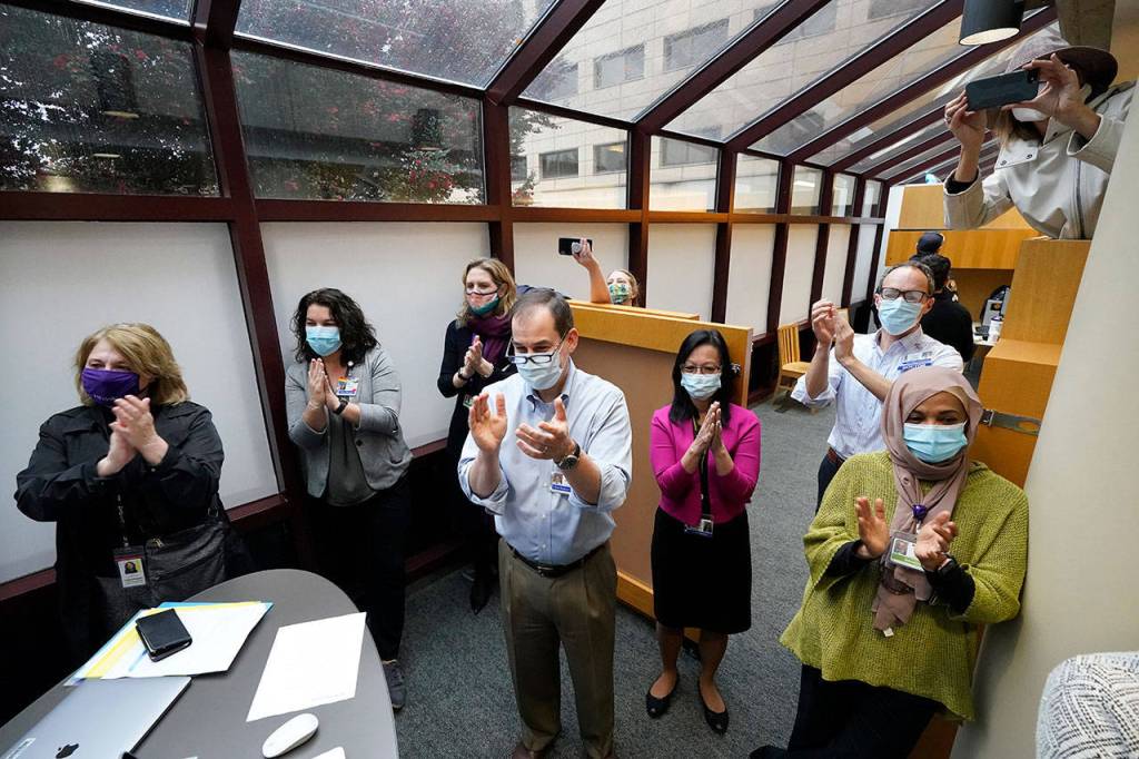 UW Medicine employees look on and applaud as the first Pfizer-BioNTech COVID-19 vaccination is completed at UW Medicine Tuesday in Seattle. (AP Photo/Elaine Thompson)