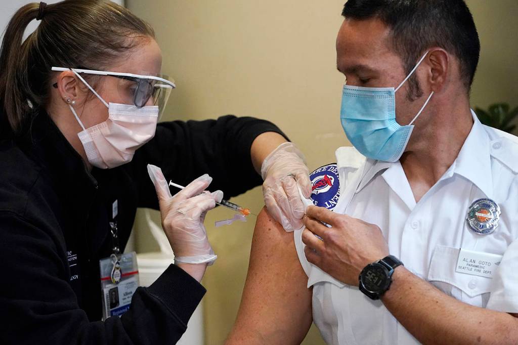Seattle Fire Department paramedic Alan Goto (right) receives one of the first Pfizer-BioNTech COVID-19 vaccinations by registered nurse Allison Miller at UW Medicine on Tuesday in Seattle. (AP Photo/Elaine Thompson)