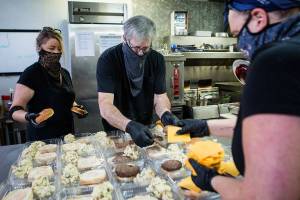 Jennifer Carlson, left to right, Jim Staniford and Katherine Stipech put together cheeseburger and potato salad meals for the Everett Gospel Mission on Thursday, Dec. 17, 2020 in Everett, Wa. (Olivia Vanni / The Herald)