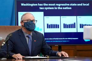 Washington Gov. Jay Inslee sits in front of a chart comparing Washington state's tax system to other western states as he talks to reporters, Thursday, Dec. 17, 2020, at the Capitol in Olympia, Wash. Inslee is proposing a new capital gains tax and a tax on health insurers as part of his two-year budget proposal that seeks to offset the revenue losses the state has seen during the ongoing coronavirus pandemic and to help bolster the state's public health system. (AP Photo/Ted S. Warren)