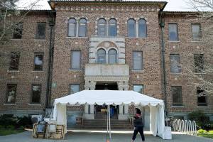 FILE - In this March 19, 2020, file photo, an employee walks near an entrance to Western State Hospital in Lakewood, Wash. As coronavirus cases top 200 in Washington state's largest psychiatric hospital, officials are implementing new procedures to try to get it under control. Making matters worse, the economic downturn that resulted from the pandemic, and the loss of revenues needed to run state government, is forcing the Department of Health and Human Services to make budget cuts, including layoffs at Western State Hospital. (AP Photo/Ted S. Warren, File)