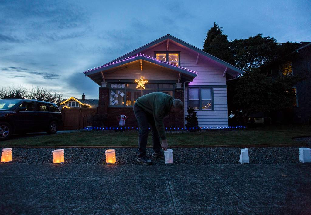 Bob Robison lights the luminaries in front of his home along the 1200 block of Rucker Avenue on Thursday, Dec. 24, 2020 in Everett, Wa. (Olivia Vanni / The Herald)