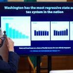 Washington Gov. Jay Inslee looks toward a chart comparing Washington state's tax system to other western states as he talks to reporters, Thursday, Dec. 17, 2020, at the Capitol in Olympia, Wash. Inslee is proposing a new capital gains tax and a tax on health insurers as part of his two-year budget proposal that seeks to offset the revenue losses the state has seen during the ongoing coronavirus pandemic and to help bolster the state's public health system. (AP Photo/Ted S. Warren)