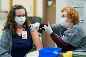 LaRae Munns, left, a nurse in the Emergency Department at Madigan Army Medical Center, receives one of the first doses of the Pfizer vaccine for COVID-19 from nurse Goldie Martin, right, Wednesday, Dec. 16, 2020, at Madigan Army Medical Center at Joint Base Lewis-McChord in Washington state, south of Seattle. Vaccinations are scheduled to continue in the coming weeks for front-line medical workers and and others in high-priority positions at the base. (AP Photo/Ted S. Warren)