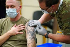 Staff Sgt. Travis Snyder, left, receives the first dose of the Pfizer vaccine for COVID-19 given at Madigan Army Medical Center at Joint Base Lewis-McChord, Wednesday, Dec. 16, 2020, in Washington state, south of Seattle. Nurse Jose Picart, right, administered the shot. Vaccinations are scheduled to continue in the coming weeks for front-line medical workers and and others in high-priority positions at the base. (AP Photo/Ted S. Warren)