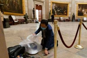 Rep. Andy Kim, D-N.J., cleans up debris and personal belongings strewn across the floor of the Rotunda in the early morning hours of Thursday, Jan. 7, 2021, after protesters stormed the Capitol in Washington, on Wednesday. (AP Photo/Andrew Harnik)