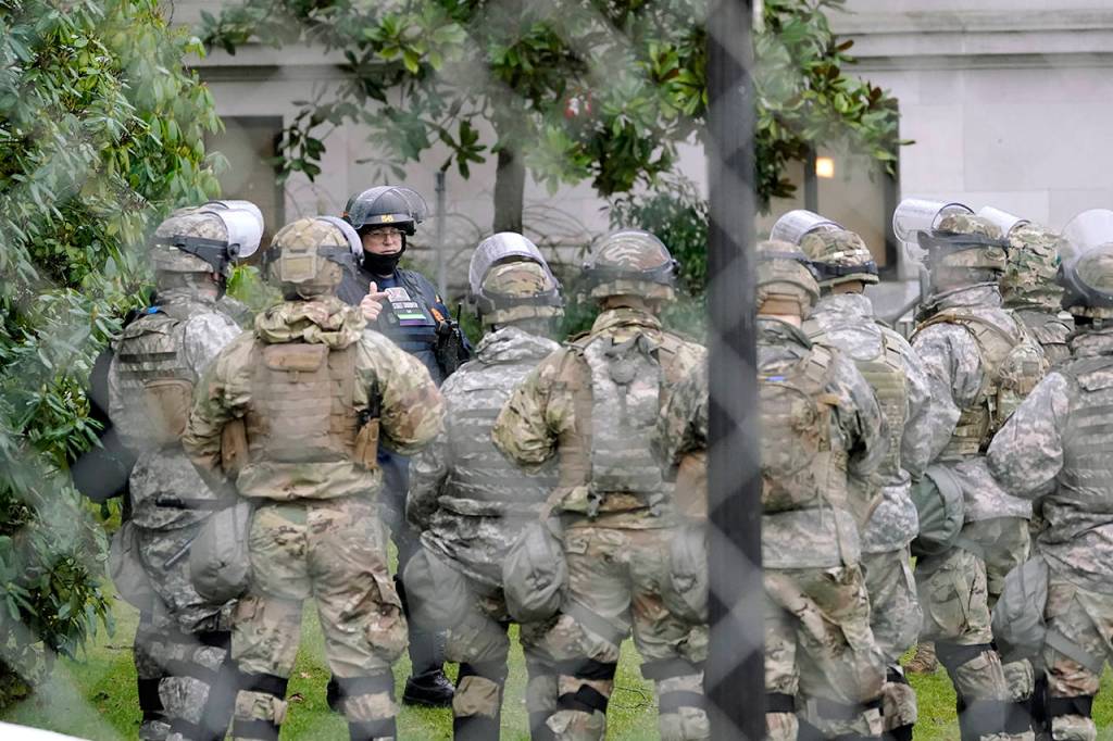 A Washington State Patrol trooper talks with members of the Washington National Guard inside a fence surrounding the Capitol in anticipation of protests Monday in Olympia. (AP Photo/Ted S. Warren)