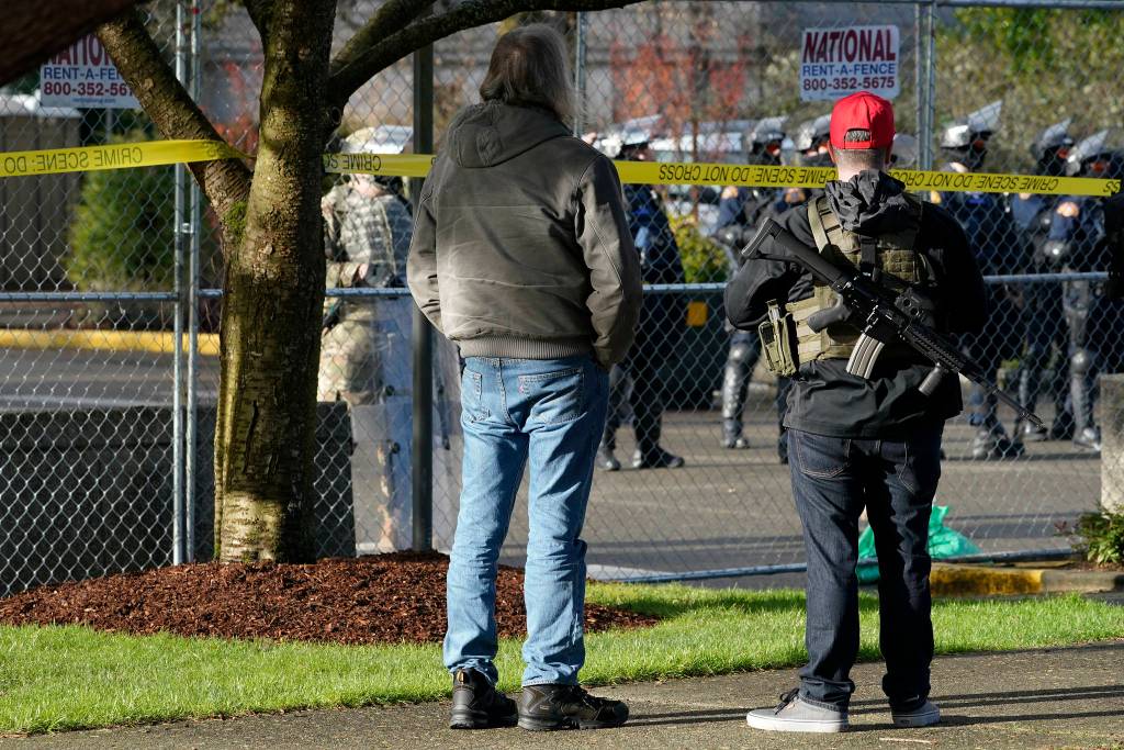 An armed supporter of President Donald Trump looks in at a gathering of Washington State Patrol troopers behind a perimeter fence Sunday during a rally at the Capitol in Olympia, Wash. Protesters from several causes rallied Sunday at the Capitol, the day before the 2021 legislative session was scheduled to begin. (AP Photo/Ted S. Warren)