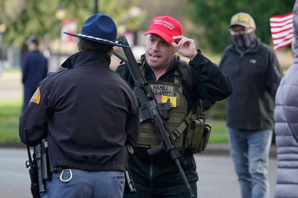 An armed supporter of President Donald Trump speaks casually with a Washington State Patrol trooper Sunday during a rally at the Capitol in Olympia, Wash. Protesters from several causes rallied Sunday at the Capitol, the day before the 2021 legislative session was scheduled to begin. (AP Photo/Ted S. Warren)