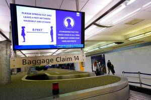FILE - In this Dec. 10, 2020, file photo, an electronic sign warns travellers to maintain social distance in the terminal of Denver International Airport in Denver.  Two airline passengers who got into disturbances after allegedly not wearing face masks now face potential fines. The Federal Aviation Administration said Friday, Dec. 18,  that it is seeking civil penalties of $15,000 and $7,500 over two separate incidents. Both happened in August.  (AP Photo/David Zalubowski, File)