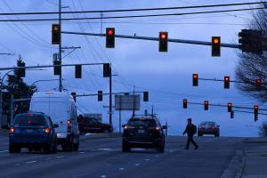 A man crosses the road under stoplights at Casino Road and Evergreen Way on Friday, Dec. 13, 2019 in Everett, Wash. The lights at Casino Road and Evergreen Way are being considered for controversial red-light traffic cameras. (Andy Bronson / The Herald)