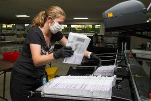 Catherine Berwicks loads ballots into a tray after scanning them at the Snohomish County Elections Ballot Processing Center on Tuesday, Aug. 4, 2020 in Everett, Wa.  (Andy Bronson / The Herald)