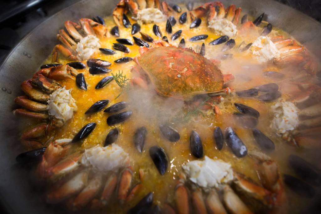 Crab and mussels cook in a large paella pan. Paella means frying pan in the Valencian language in Spain. (Olivia Vanni / The Herald)