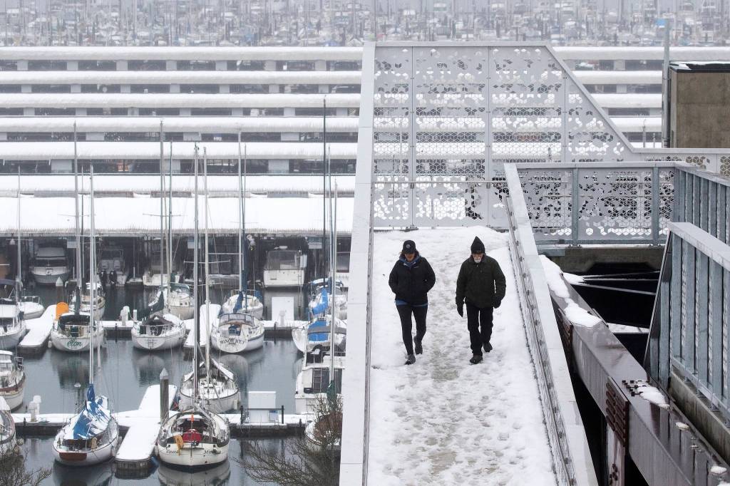 As rain begin to melt snow on boats Monday at the Port of Everett Marina, a couple walks down the Grand Avenue Park Bridge in Everett. (Andy Bronson / The Herald)