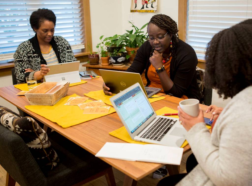 Carissa Walker (left), Mamouna Fame and Avianca Walker-Loundermon talk about the event calendar, one feature of their Black SnoCo venture, on Feb. 23 in Everett. (Olivia Vanni / The Herald)