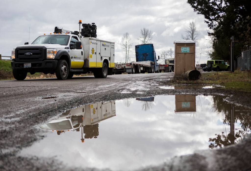 Trucks drive by large puddles and potholes along 40th Avenue NE on Friday in Marysville. (Olivia Vanni / The Herald)