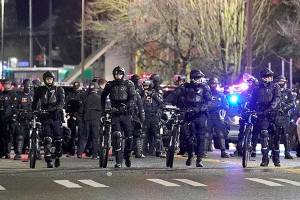 Tacoma Police and other law enforcement officials stand in a line as protesters approach in the street in front of the City-County Building during a protest against police brutality, late Sunday, Jan. 24, 2021, in downtown Tacoma, Wash., south of Seattle. The protest came a day after at least two people were injured when a Tacoma Police officer responding to a report of a street race drove his car through a crowd of pedestrians that had gathered around him. Several people were knocked to the ground and at least one person was run over. (AP Photo/Ted S. Warren)
