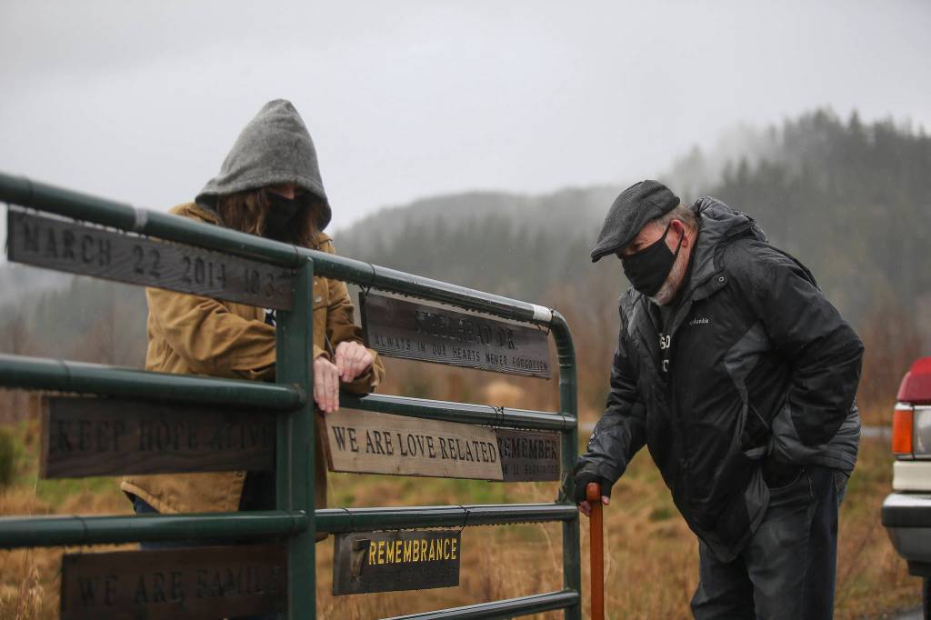 Jennifer Thompson tightens a sign made by her father, Ron Thompson, who placed it on the gate entrance to Oso Memorial Park. Ron Thompson makes a new sign every year. (Andy Bronson / The Herald)
