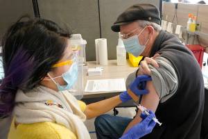 Substitute teacher Oscar Gardner, 76, right, gets the first dose of the Moderna COVID-19 vaccine from Kim Vo, left, a pharmacist working for the Seattle Indian Health Board, Monday, March 15, 2021, at a SIHB clinic in Seattle. The SIHB began vaccinating front line staff from Seattle Public Schools Monday, including substitute teachers, custodians, nutrition services staff, special education teachers, and instructional aides, after determining they had enough doses of the vaccine to share with school workers. (AP Photo/Ted S. Warren)