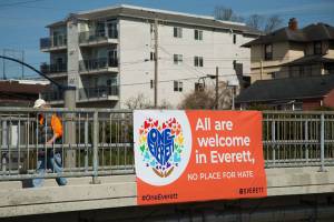 A man walks by a sign on the 25th Street pedestrian bridge on Wednesday, March 31, 2021 in Everett, Washington. The City of Everett posted the sign in response to an earlier sign that read "Reclaim America" which was removed by the city and replaced with a sign that reads "All are welcome in Everett, no place for hate."  (Andy Bronson / The Herald)