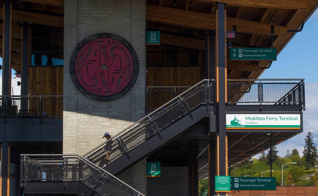 A woman walks down steps under artwork by Tulalip artist and master carver Joe Gobin at the Mukilteo ferry terminal on Monday. (Andy Bronson / The Herald)
