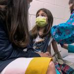 In this Wednesday, March 24, 2021 image from video provided by Duke Health, Alejandra Gerardo, 9, looks up to her mom, Dr. Susanna Naggie, as she gets the first of two Pfizer COVID-19 vaccinations during a clinical trial for children at Duke Health in Durham, N.C. In the U.S. and abroad, researchers are beginning to test younger and younger kids, to make sure the shots are safe and work for each age. (Shawn Rocco/Duke Health via AP)