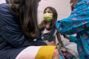 In this Wednesday, March 24, 2021 image from video provided by Duke Health, Alejandra Gerardo, 9, looks up to her mom, Dr. Susanna Naggie, as she gets the first of two Pfizer COVID-19 vaccinations during a clinical trial for children at Duke Health in Durham, N.C. In the U.S. and abroad, researchers are beginning to test younger and younger kids, to make sure the shots are safe and work for each age. (Shawn Rocco/Duke Health via AP)