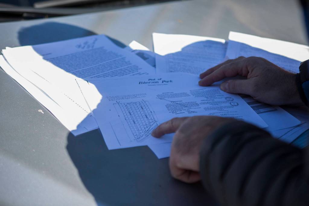 Chris Woytko shows documents that detail ownership of lots along East Ibberson Drive and West Ibberson Drive, a narrow loop along Silver Lake in Everett, on March 10. (Olivia Vanni / The Herald)