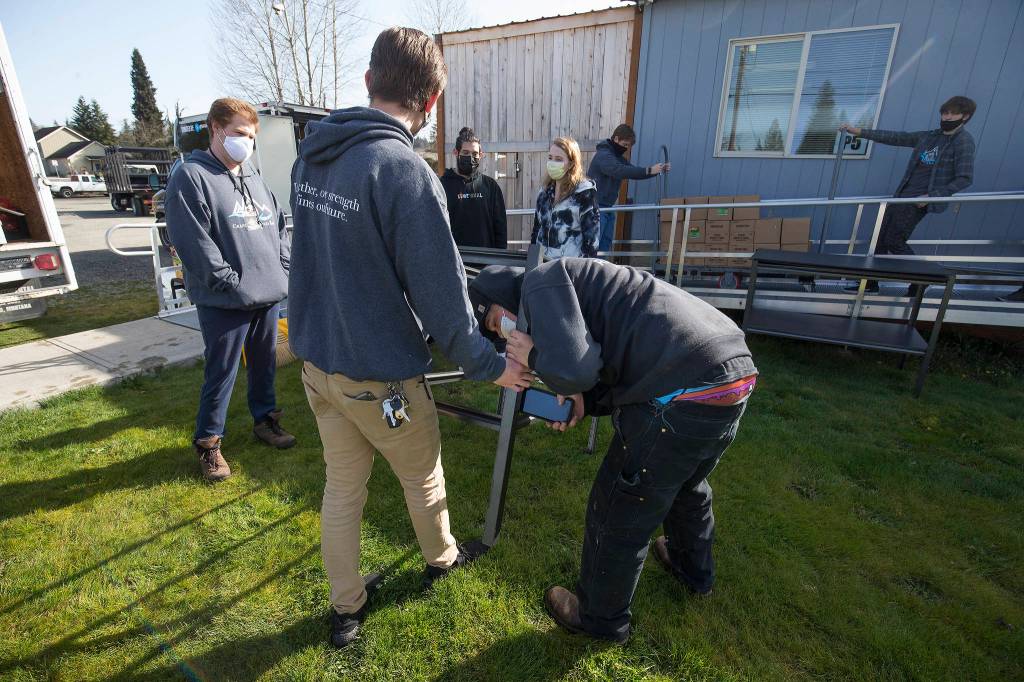 Dawson McTear uses his cellphone to pound a shelf bar into place as he and others help move the Granite Falls Food Bank from its old location to a new one Tuesday. (Andy Bronson / The Herald)