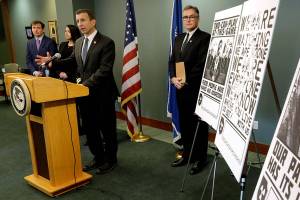 Raymond Duda, FBI Special Agent in Charge in Seattle, speaks during a news conference at a podium at left, Wednesday, Feb. 26, 2020, about charges against a group of alleged members of the neo-Nazi group Atomwaffen Division for cyber-stalking and mailing threatening communications — including the Swastika-laden posters at right — in a campaign against journalists in several cities. (AP Photo/Ted S. Warren)
