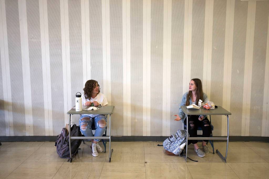 Mia Luscher (left) and Makena Limb chat in the cafeteria during the first day of in-person school for Everett High students. (Andy Bronson / The Herald)