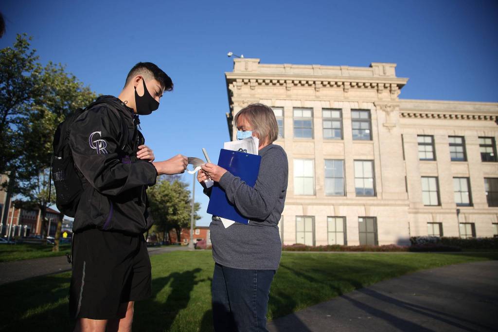 Ryan Sanchez gets a wristband from Barbara Lichneckert on Monday before entering Everett High for the first time this year. (Andy Bronson / The Herald)