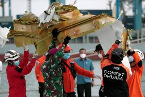 Rescuers carry a part of aircraft recovered from Java Sea where a Sriwijaya Air passenger jet crashed, at Tanjung Priok Port in Jakarta, Indonesia, Monday, Jan. 11, 2021. The search for the black boxes of a crashed Sriwijaya Air jet intensified Monday to boost the investigation into what caused the plane carrying dozens of people to nosedive at high velocity into the Java Sea. (AP Photo/Dita Alangkara)