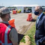 Gov. Jay Inslee speaks with pod manager Peyton Plucker at the mass vaccination site at Arlington Municipal Airport on Tuesday. (Olivia Vanni / The Herald)