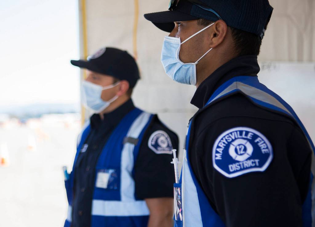 Marysville firefighters listen to Gov. Jay Inslee at the COVID-19 vaccination site at Arlington Municipal Airport on Tuesday. (Olivia Vanni / The Herald)