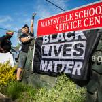 Gus Underfoot hangs a Black Lives Matter flag underneath the Marysville School District sign during a protest on Wednesday. (Olivia Vanni / The Herald)