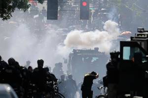 FILE - In this July 25, 2020, file photo, smoke rises as police clash with protester during a Black Lives Matter protest near the Seattle Police East Precinct headquarters in Seattle. A Seattle police officer who threw a tear gas canister that hit a reporter and other officers who threw blast balls that hit individuals during last summer's Black Lives Matter protests violated policies, according to new reports from an independent agency tasked with investigating police misconduct. The agency has released five batches of investigative reports since September, with the latest 22 cases posted Friday, Jan. 15, 2021. (AP Photo/Ted S. Warren, File)