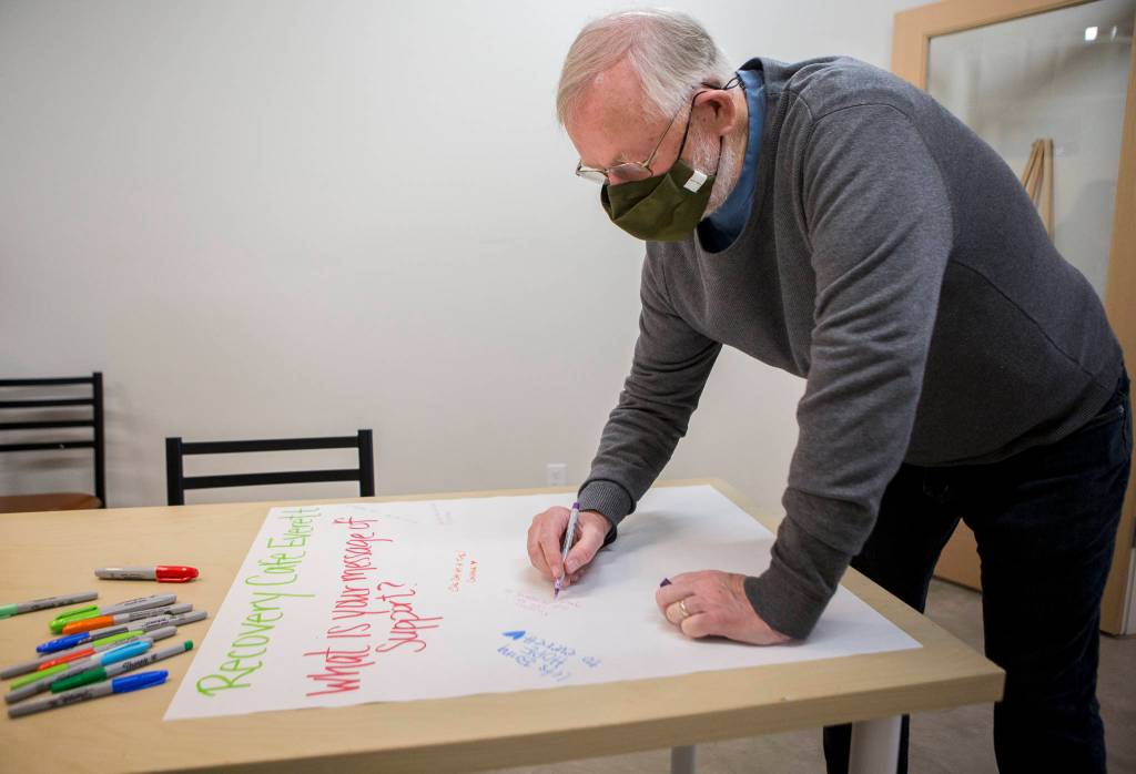 Ed Petersen writes words of support on a banner in a new art and meeting room at the Everett Recovery Cafe grand opening on Wednesday. (Olivia Vanni / The Herald)