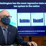 Washington Gov. Jay Inslee sits in front of a chart comparing Washington state's tax system to other western states as he talks to reporters, Thursday, Dec. 17, 2020, at the Capitol in Olympia, Wash. Inslee is proposing a new capital gains tax and a tax on health insurers as part of his two-year budget proposal that seeks to offset the revenue losses the state has seen during the ongoing coronavirus pandemic and to help bolster the state's public health system. (AP Photo/Ted S. Warren)