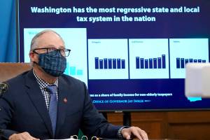 Washington Gov. Jay Inslee sits in front of a chart comparing Washington state's tax system to other western states as he talks to reporters, Thursday, Dec. 17, 2020, at the Capitol in Olympia, Wash. Inslee is proposing a new capital gains tax and a tax on health insurers as part of his two-year budget proposal that seeks to offset the revenue losses the state has seen during the ongoing coronavirus pandemic and to help bolster the state's public health system. (AP Photo/Ted S. Warren)