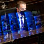 Gary Holt, who reads bills being considered in the Washington House, wears a mask as he sits behind a plexiglass shield with reflections of state representatives meeting remotely on it, Wednesday, April 21, 2021, at the Capitol in Olympia Wash. The House was considering a proposed new tax in Washington state on capital gains that would be imposed on the sale of stocks and bonds in excess of $250,000. (AP Photo/Ted S. Warren)