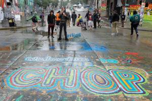FILE - In this June 30, 2020, file photo, a sign on the street reads "Welcome to CHOP" as protesters stand near barricades, at the CHOP (Capitol Hill Occupied Protest) zone in Seattle. The area, which was also known as CHAZ, was occupied for several weeks during the summer by protesters after Seattle Police pulled back from their East Precinct building following violent clashes with demonstrators. (AP Photo/Ted S. Warren, File)