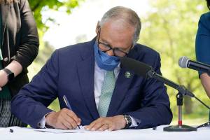 Washington Gov. Jay Inslee signs a bill into law, Tuesday, May 4, 2021, in Tukwila, Wash., that levies a new capital gains tax on high profit stocks, bonds and other assets for some residents of Washington state. (AP Photo/Ted S. Warren)