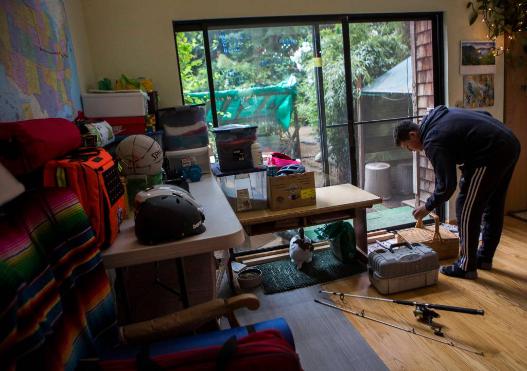 Deven Boyce adds a fishing pole and tackle box to a supply pile in preparation for his cross-country bike ride. (Olivia Vanni / The Herald)