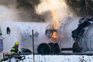 A firefighter sprays foam on burning, derailed train cars Tuesday, Dec. 22, 2020, in Custer, Wash. Officials say seven train cars carrying crude oil derailed and five caught fire north of Seattle and close to the Canadian border. Whatcom County officials said the derailment occurred in the downtown Custer area, where streets were closed and evacuations ordered during a large fire response. (AP Photo/Elaine Thompson)