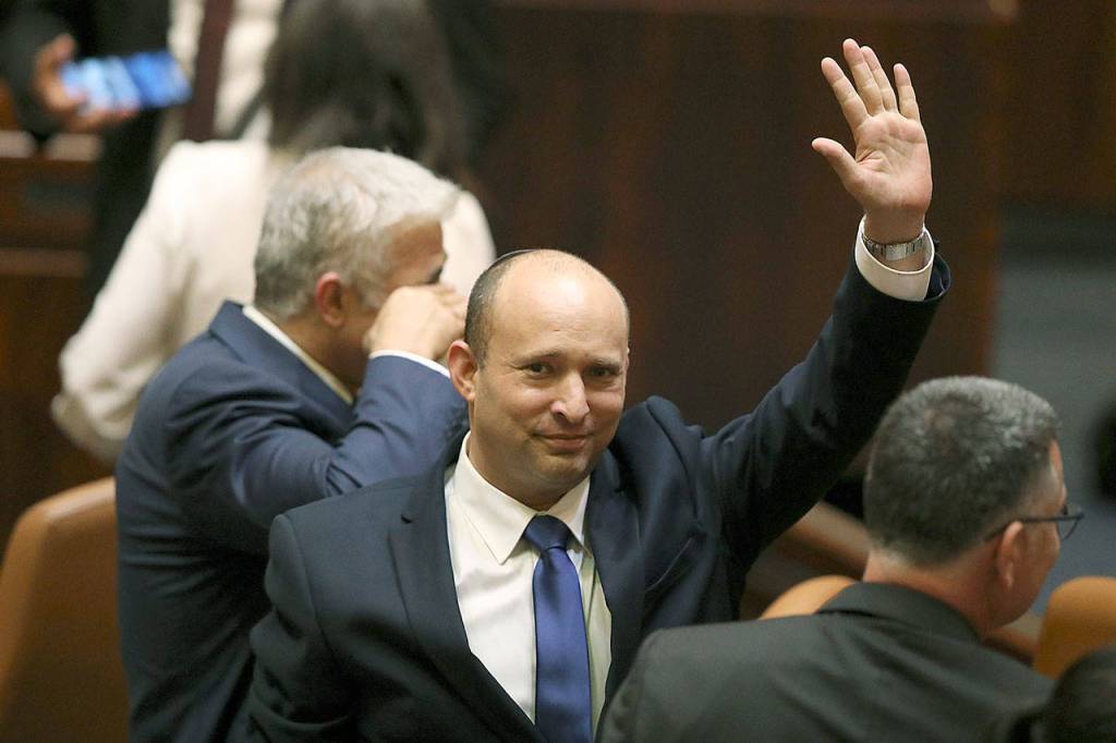 Israels new prime minister Naftali Bennett raises his hand Sunday during a Knesset session in Jerusalem. Israels parliament has voted in favor of a new coalition government, formally ending Prime Minister Benjamin Netanyahus historic 12-year rule. Naftali Bennett, a former ally of Netanyahu became the new prime minister. (AP Photo/Ariel Schalit)