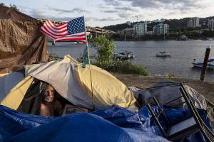 Frank, a homeless man sits in his tent with a river view in Portland, Ore., on Saturday, June 5, 2021. Until a year ago, the city was best known nationally for its ambrosial food scene, craft breweries and “Portlandia” hipsters. Now, months-long protests following the killing of George Floyd, a surge in deadly gun violence, and an increasingly visible homeless population have many questioning whether Oregon’s largest city can recover. (AP Photo/Paula Bronstein)