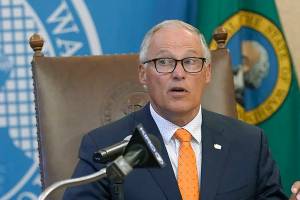 Washington Gov. Jay Inslee glances at an aide holding up an image of a visual slide being shown to viewers of a news conference, Thursday, June 3, 2021, in Olympia, Wash. Inslee announced that Washington will be the latest state to offer prizes to encourage people to get vaccinated against COVID-19. Incentives will include a series of giveaways during the month of June including lottery prizes totaling $2 million, college tuition assistance, airline tickets, and game systems. (AP Photo/Ted S. Warren)