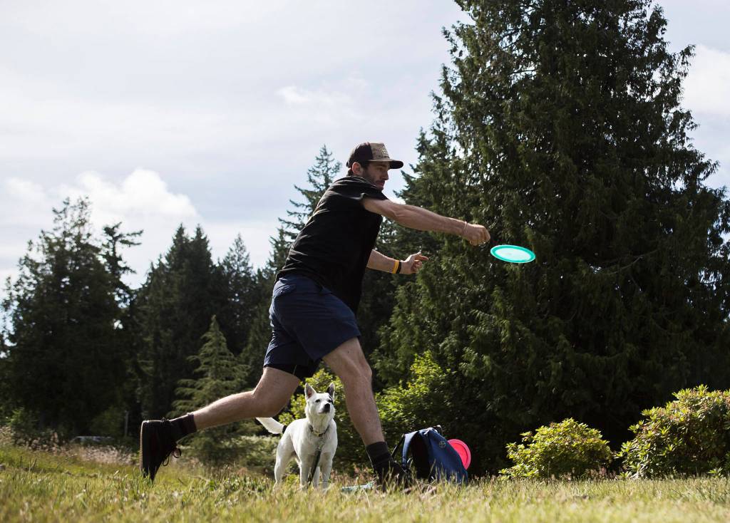 James Schneider and his dog Lily tee off at Kayak Point Disc Golf Resort on Friday, June 18, 2021 in Stanwood, Wa. (Olivia Vanni / The Herald)