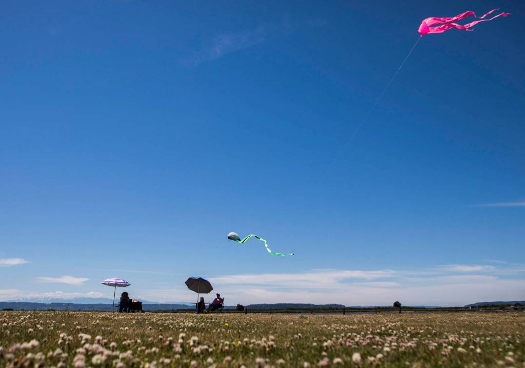 Ann Ottini (left) and Joanne Smith sit under beach umbrellas while flying kites at Boxcar Park on Thursday in Everett. (Olivia Vanni / The Herald)